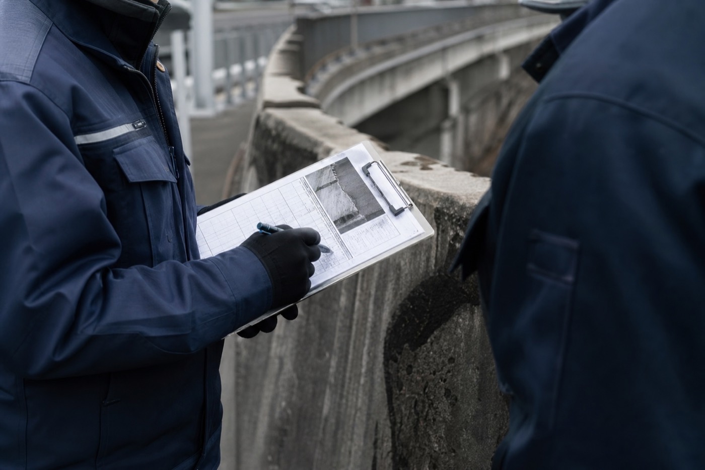 橋の高欄脇で点検記録を確認する技術者